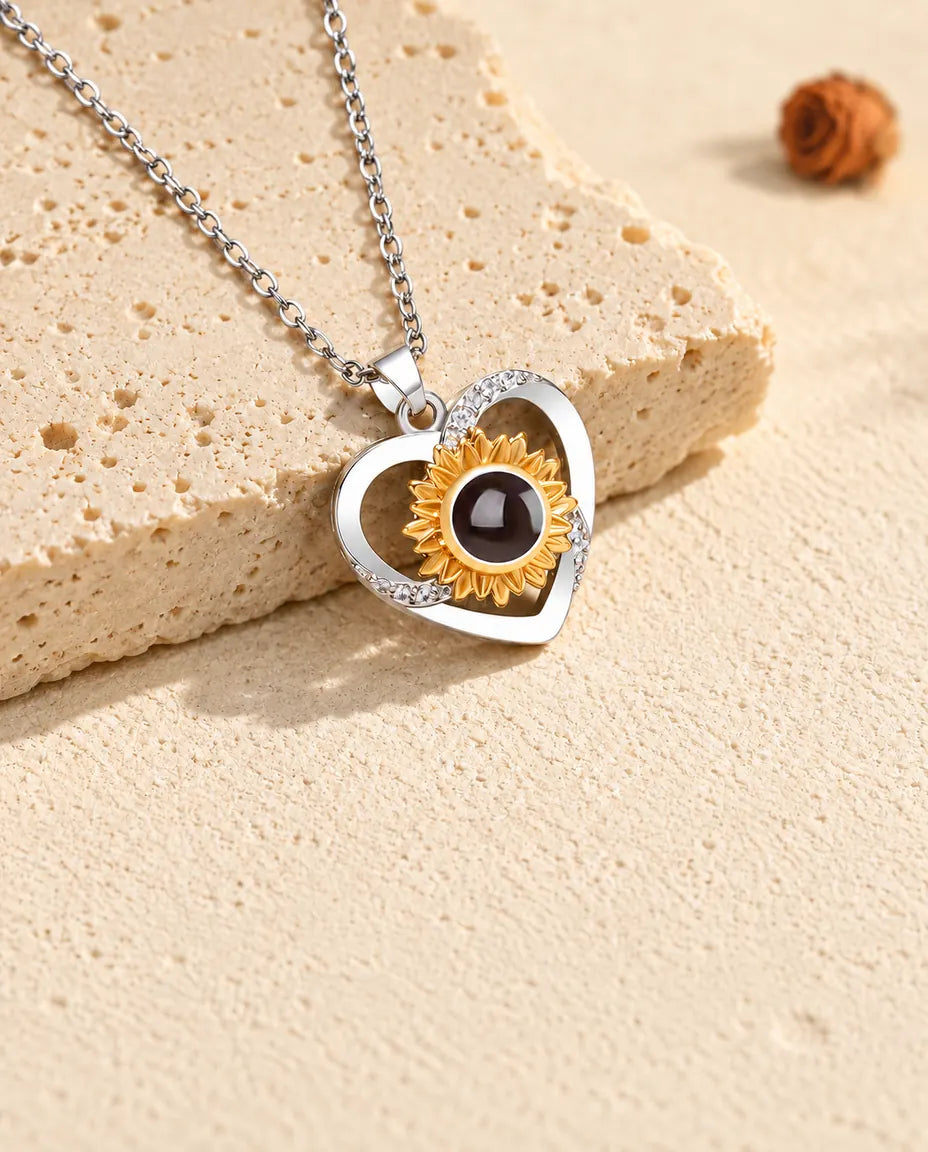 Collar de corazón con girasol y foto dentro, inclinado junto a una losa de travertino