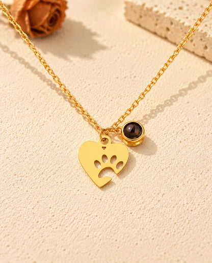 Vista frontal del collar dorado de corazón con huella y su bolita de proyección