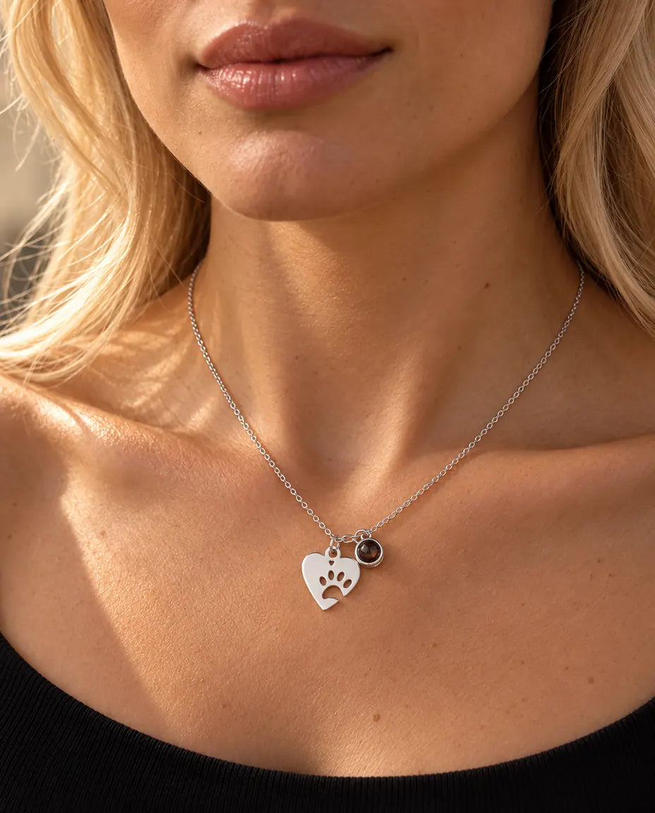 Mujer con un top negro de punto luciendo el collar plateado de corazón con huella y foto de mascota