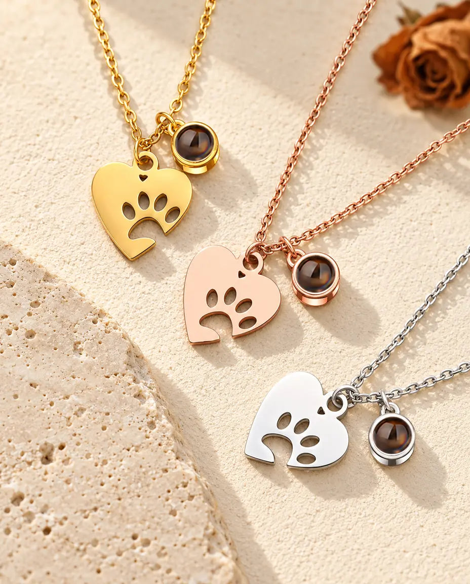 Collares de corazón con huella en dorado, color oro rosa y plateado, junto a una losa de travertino