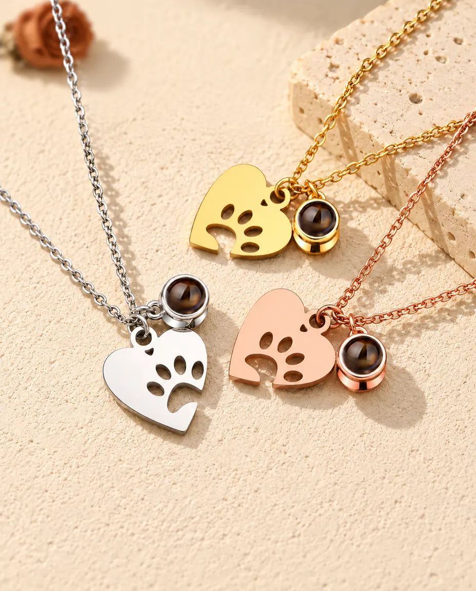 Collares de corazón con huella plateado, dorado y color oro rosa, dispuestos junto a una losa de travertino