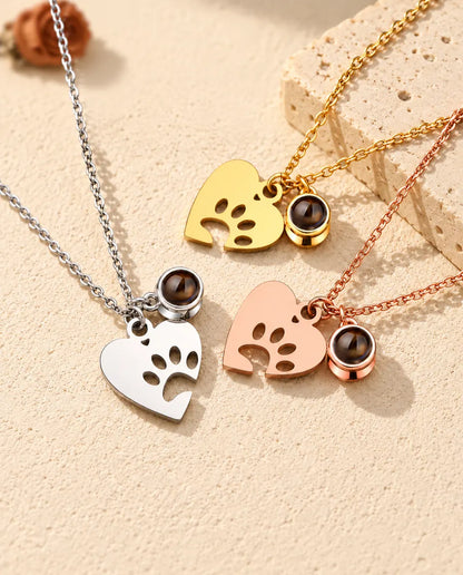Collares de corazón con huella plateado, dorado y color oro rosa, dispuestos junto a una losa de travertino