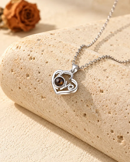 Collar con foto dentro plateado de corazón Love con un arco de circonitas, apoyado en un bloque de travertino