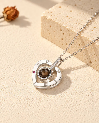 Collar con foto dentro de plata de ley 925 con corazón de números romanos, sobre yeso crema junto a un travertino