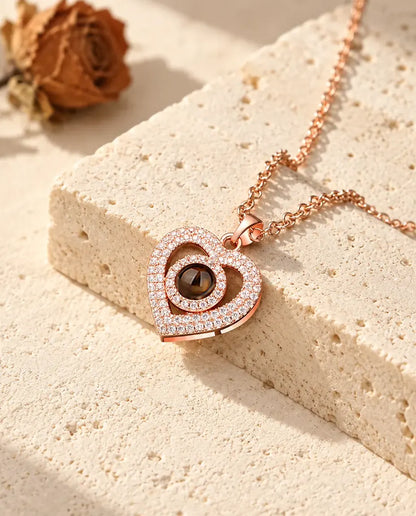 Colgante color oro rosa de doble corazón con circonitas, apoyado en un bloque de travertino