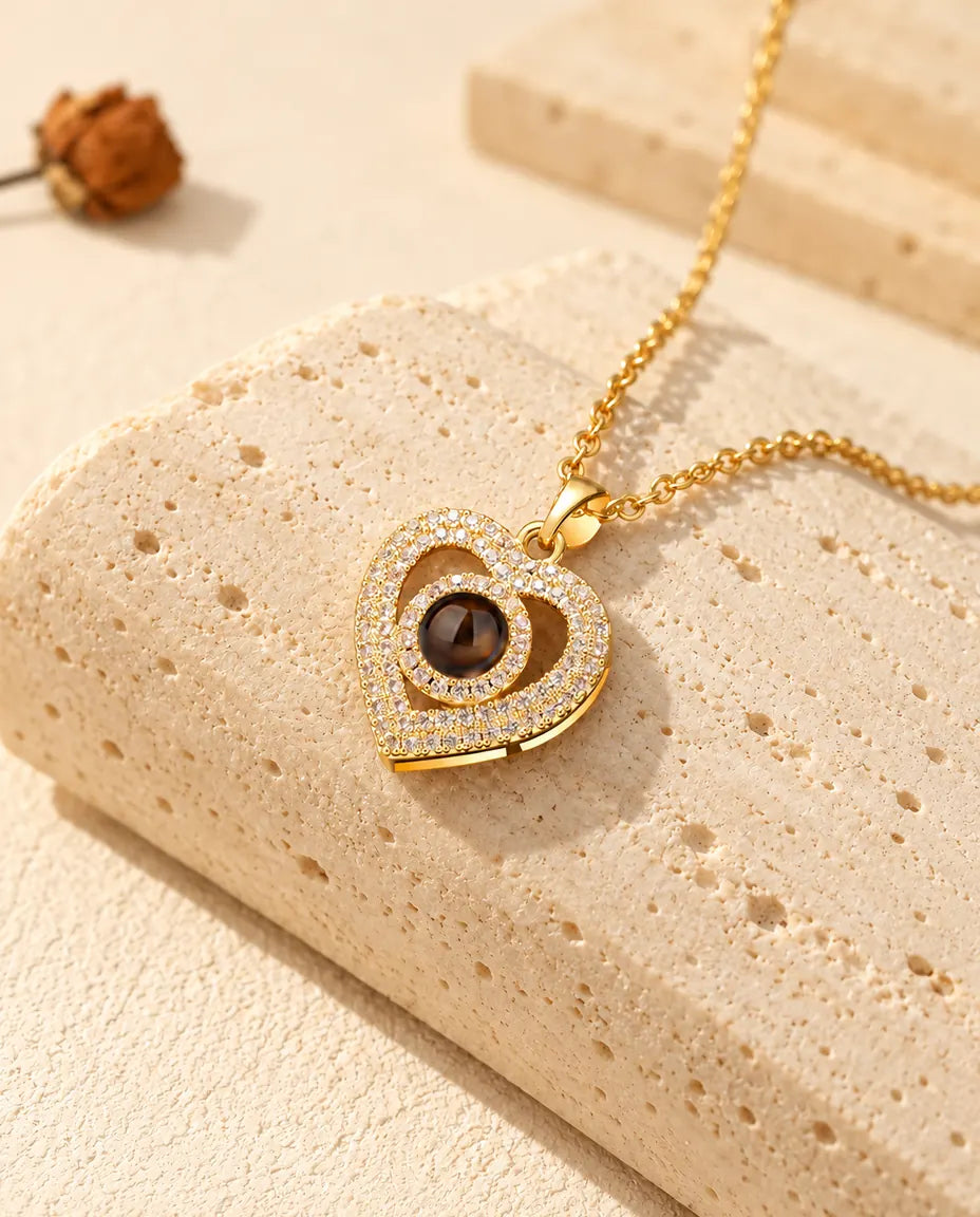 Collar dorado de doble corazón con la bola de proyección en el centro, sobre travertino