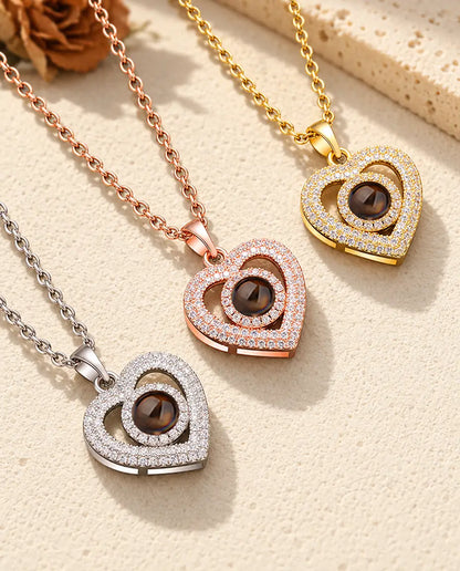 Los tres colores del collar de doble corazón con foto dentro, en diagonal sobre yeso color crema