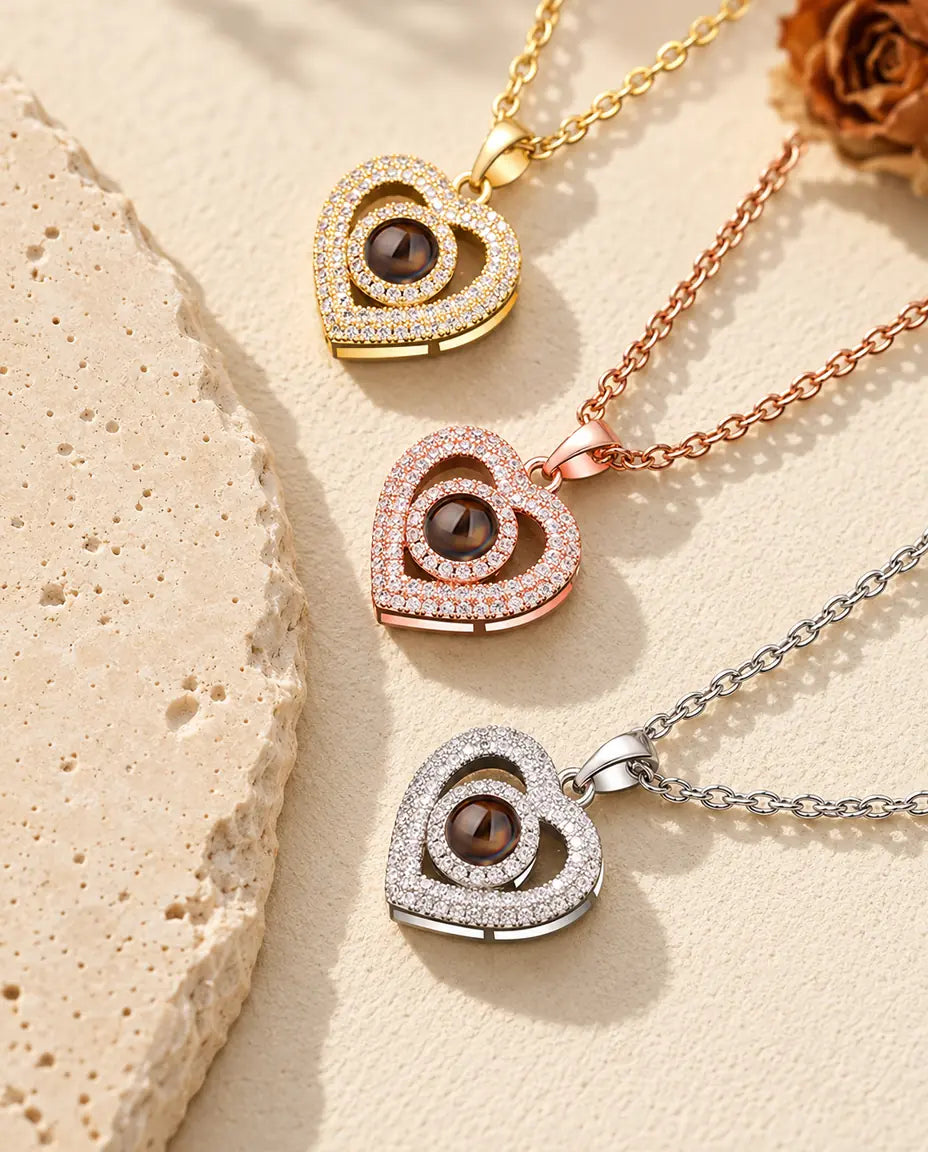 Colgantes de doble corazón en dorado, color oro rosa y plateado, apilados junto a una losa de travertino