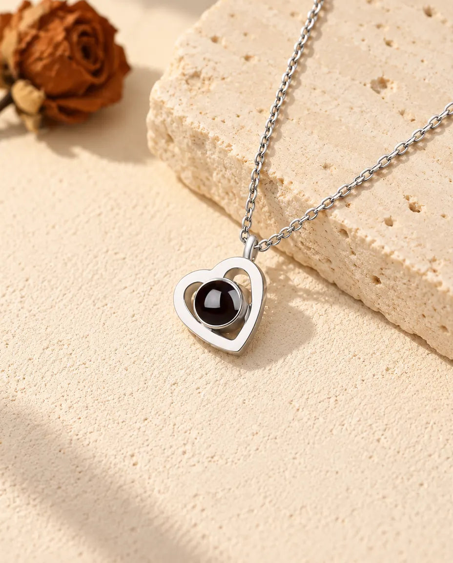 Collar con foto dentro de doble corazón en plata de ley 925 sobre yeso crema, junto a un bloque de travertino