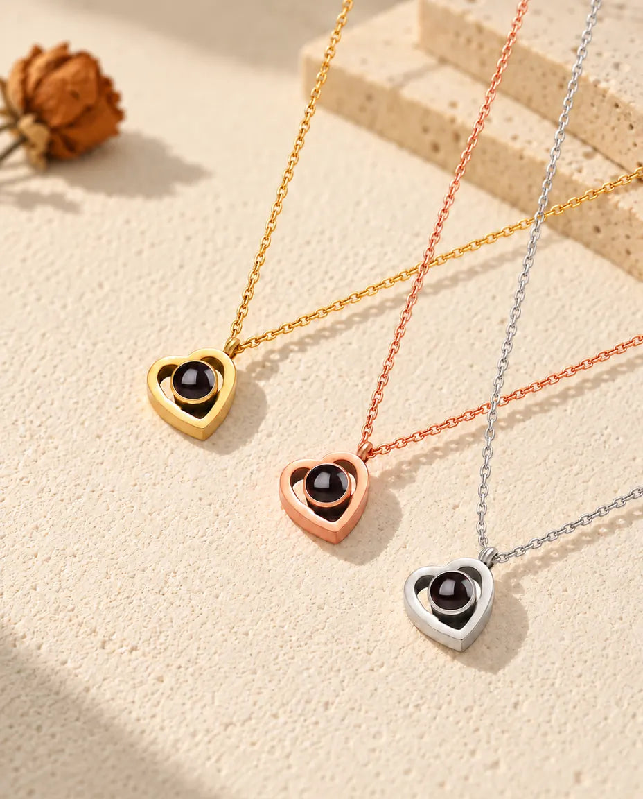 Collares de doble corazón con foto dentro en dorado, color oro rosa y plata, colocados en diagonal sobre yeso