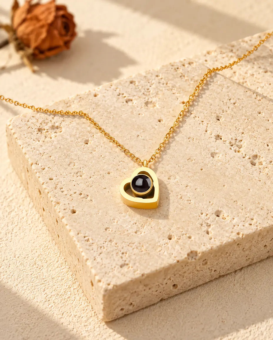 Collar de doble corazón dorado con foto dentro, tumbado sobre un bloque de travertino