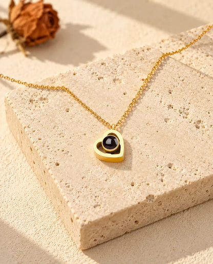 Collar de doble corazón dorado con foto dentro, tumbado sobre un bloque de travertino