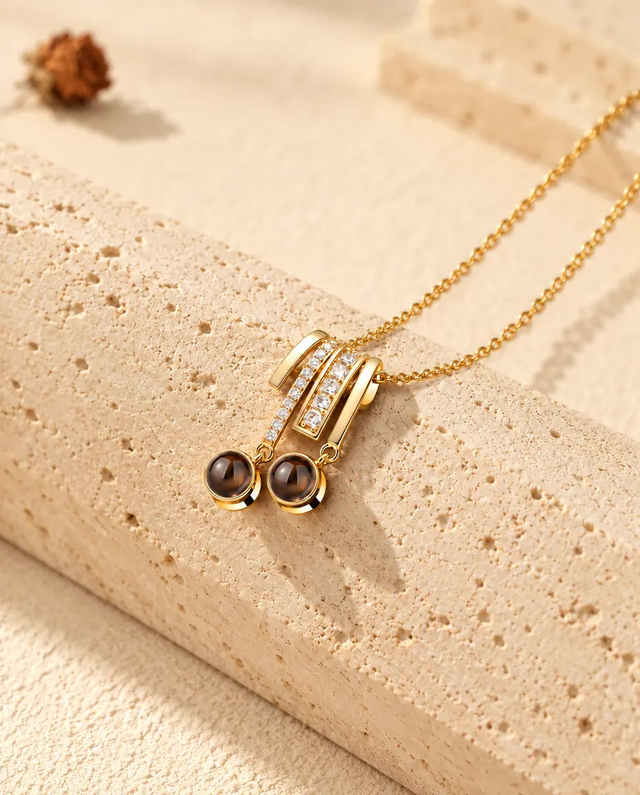 Collar dorado con colgante de circonitas y dos bolas redondas de proyección, apoyado sobre travertino