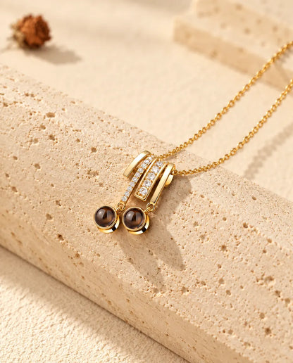 Collar dorado con colgante de circonitas y dos bolas redondas de proyección, apoyado sobre travertino