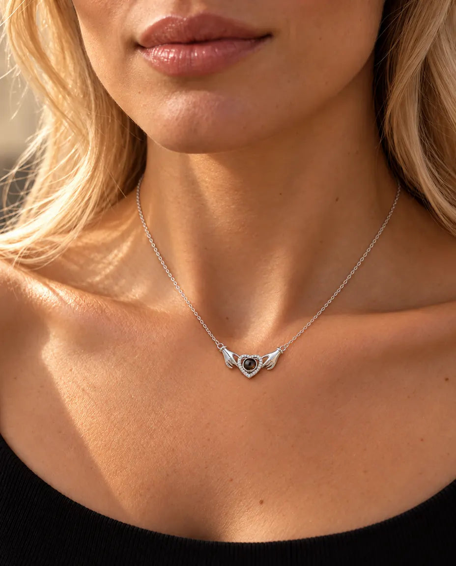Mujer con un top negro de punto luciendo el collar plateado de dos manos con corazón y foto dentro