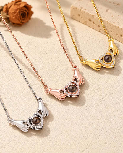 Collares de manos sujetando un corazón en plateado, color oro rosa y dorado, colocados uno junto a otro