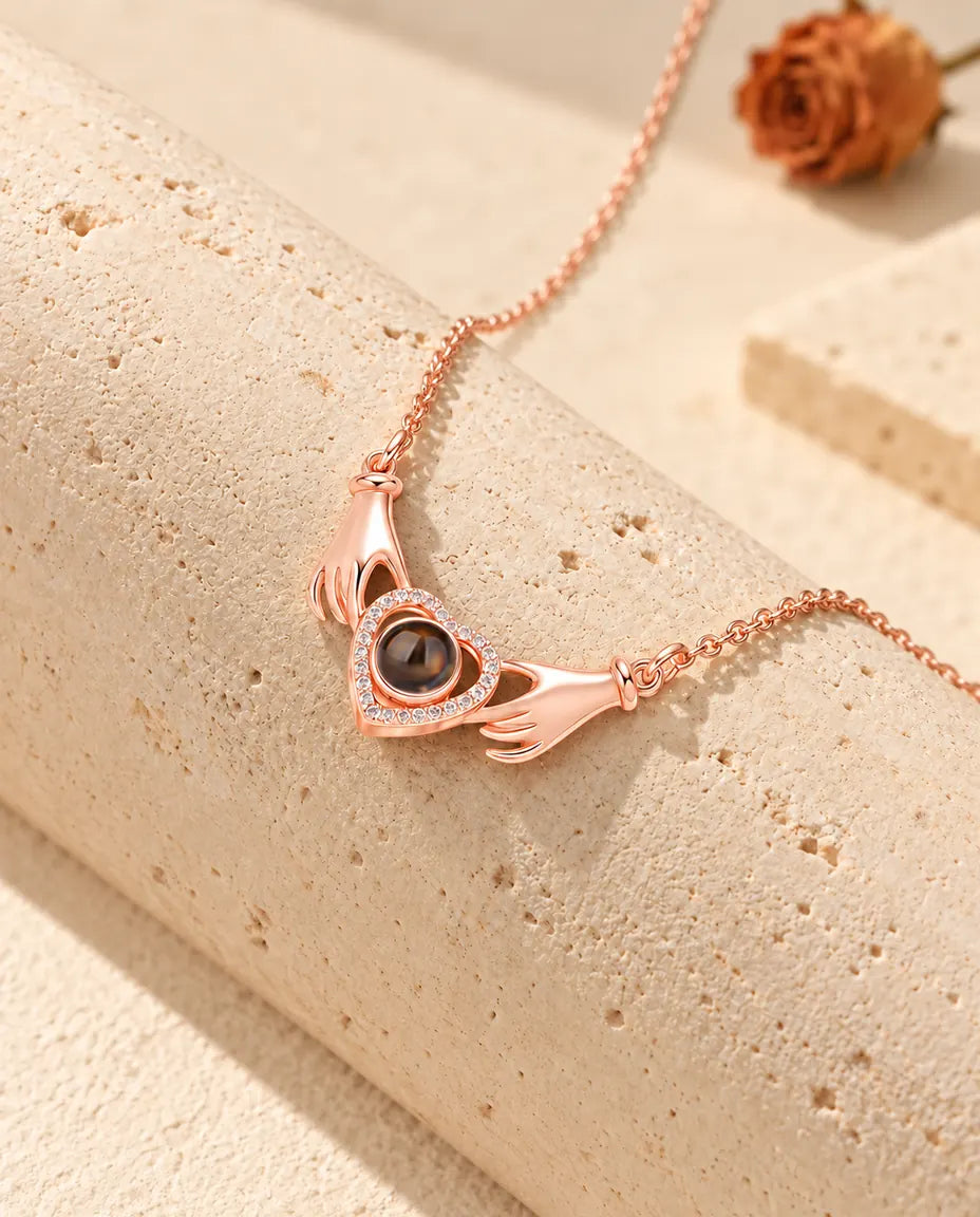 Collar color oro rosa de dos manos con corazón y foto dentro, colgado sobre un bloque de travertino