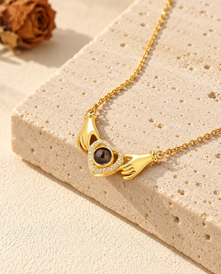 Collar dorado con foto dentro de dos manos que sujetan un corazón de circonitas, sobre travertino