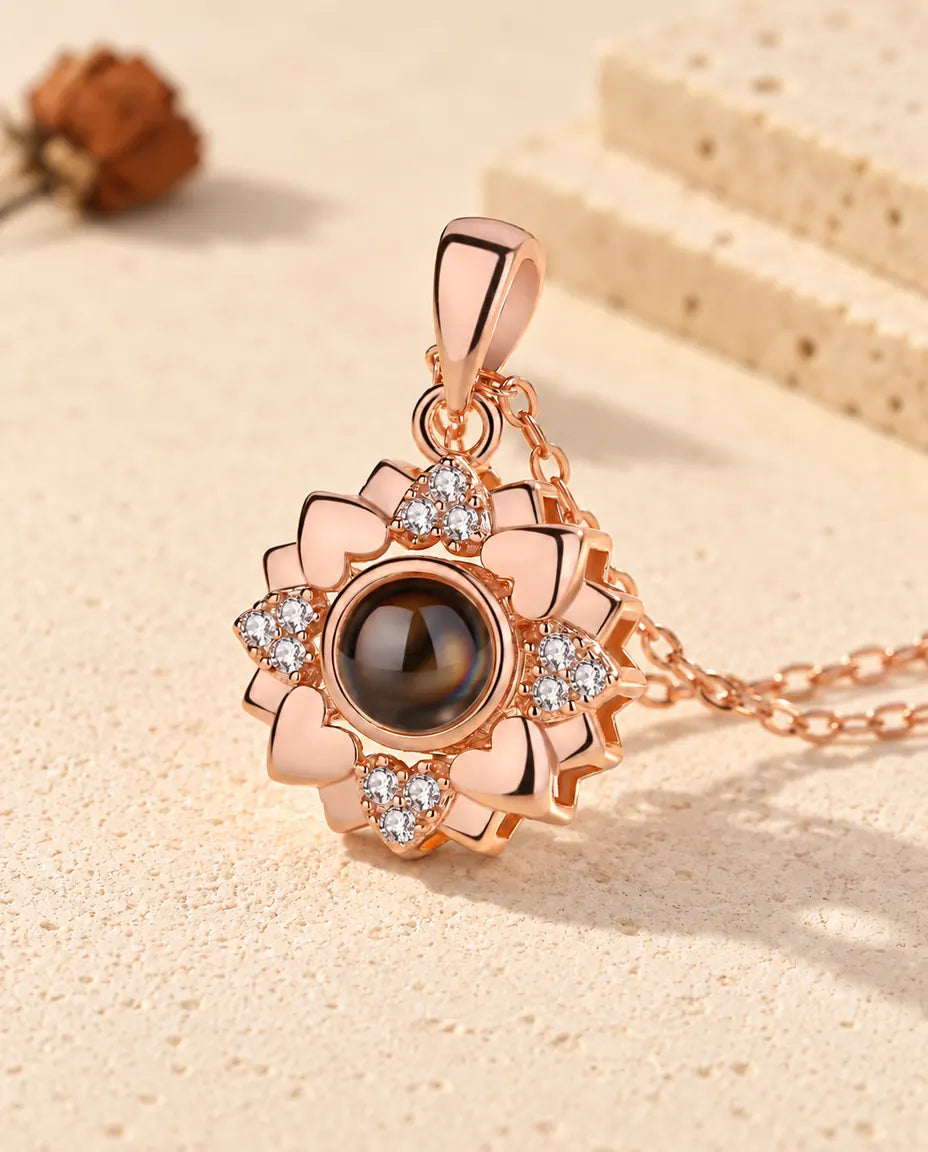 Collar con foto dentro en color oro rosa con flor de corazones y circonitas, sobre yeso color crema