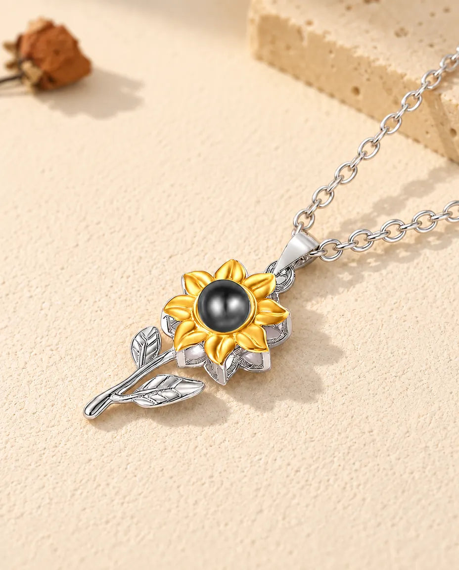 Colgante de girasol de plata con dos hojas y foto dentro, tumbado sobre yeso
