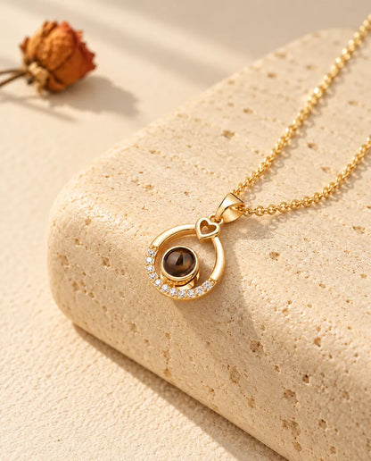 Collar con foto dentro de gota dorado, con un pequeño corazón arriba, sobre travertino