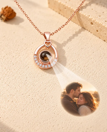 Collar de gota en color oro rosa que proyecta la foto de una pareja sobre yeso crema