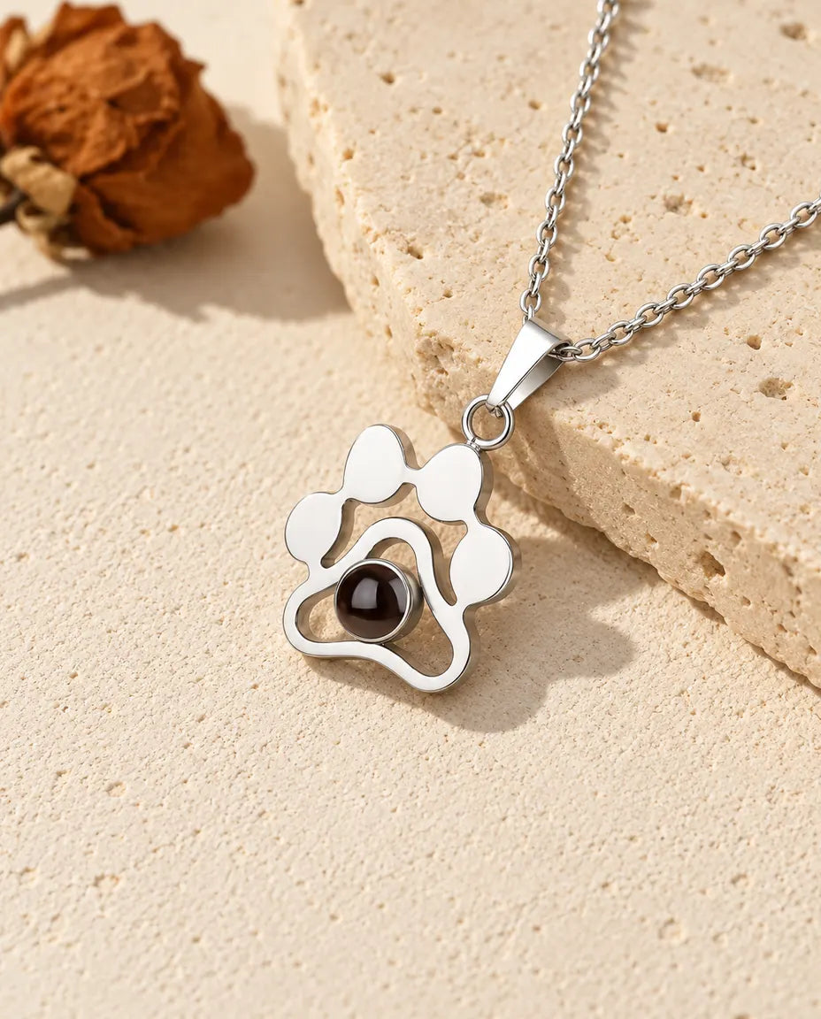 Collar con foto dentro de plata de ley 925 con huella de patita, apoyado sobre una losa de travertino