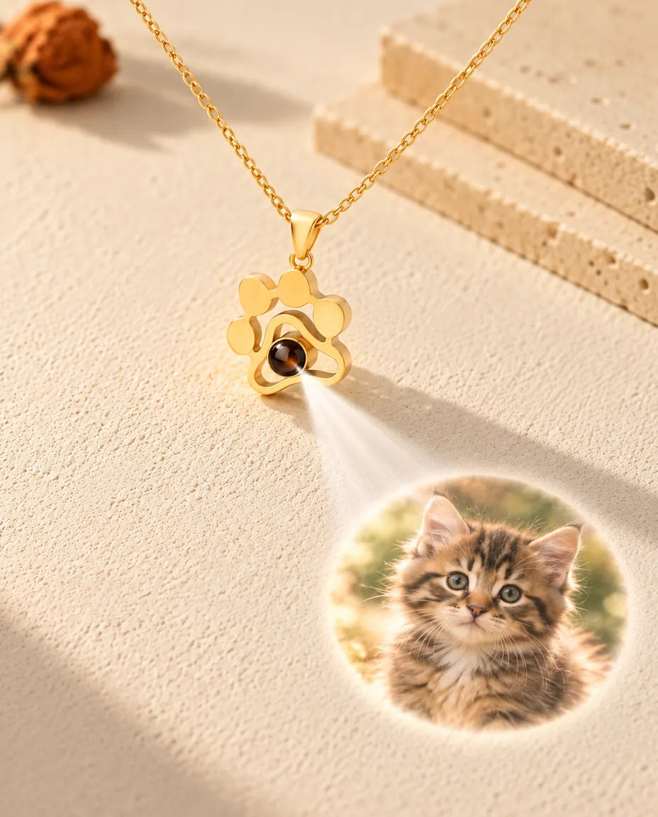 Collar de huella dorado cuya bola muestra la foto de un gatito sobre yeso color crema