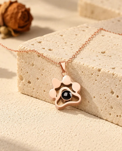 Collar de huella con foto dentro en color oro rosa, colgado sobre un bloque de travertino