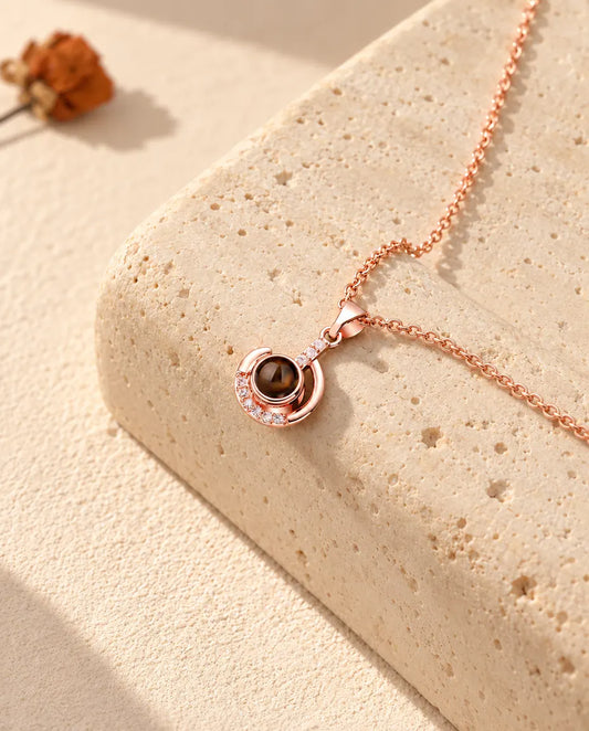 Collar con foto dentro de luna creciente en color oro rosa, sobre un bloque de travertino