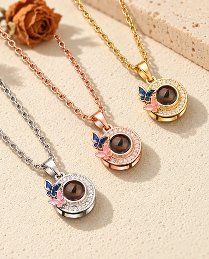Los tres colores del collar de mariposas con foto dentro, en diagonal sobre yeso color crema
