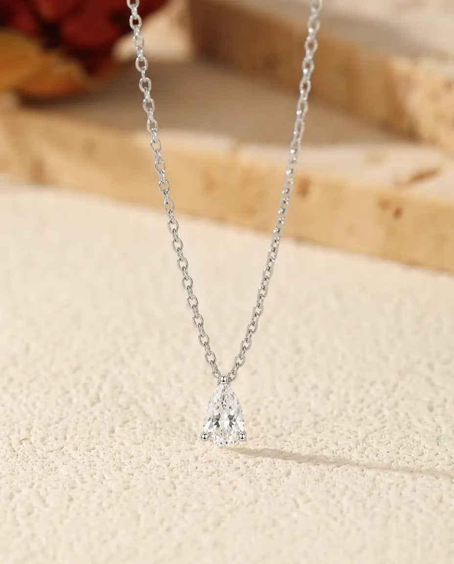 Collar de Moissanita Pera 1 ct en Plata 925 - colgante sobre una superficie clara junto a una losa de travertino