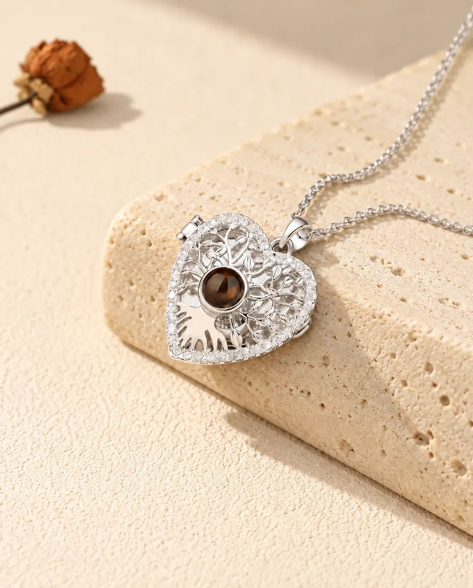 Collar relicario de corazón con árbol de la vida en plateado y bola marrón, apoyado en un bloque de travertino