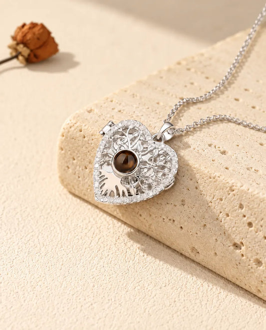 Collar relicario de corazón con árbol de la vida en plateado y bola marrón, apoyado en un bloque de travertino