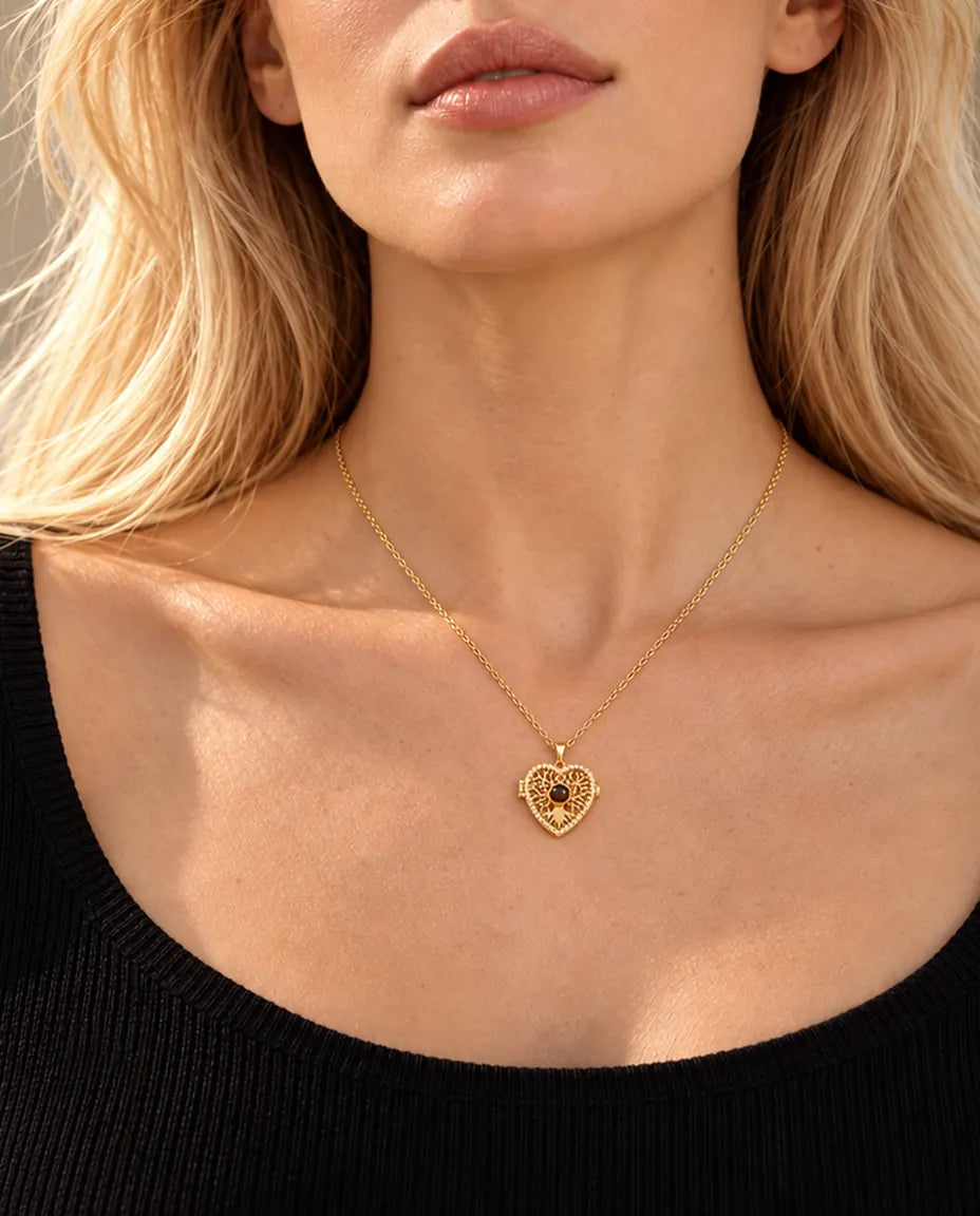 Mujer rubia con un top negro que lleva el collar relicario dorado de corazón con árbol de la vida y bola central