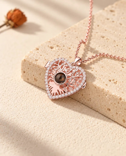 Collar relicario de corazón con árbol de la vida en color oro rosa, colgado sobre un bloque de travertino