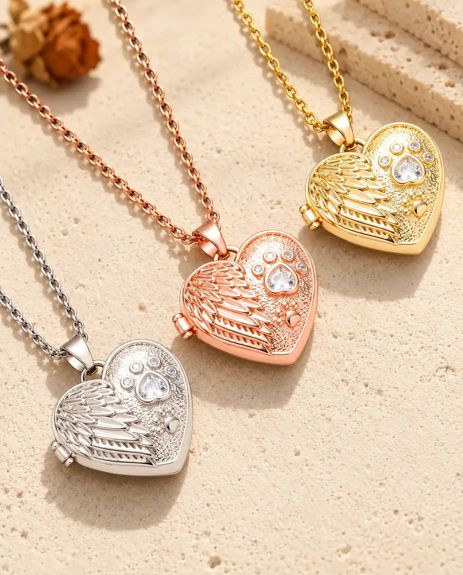 Tres relicarios con ala de ángel y huella, plateado, color oro rosa y dorado, colocados en diagonal sobre yeso crema