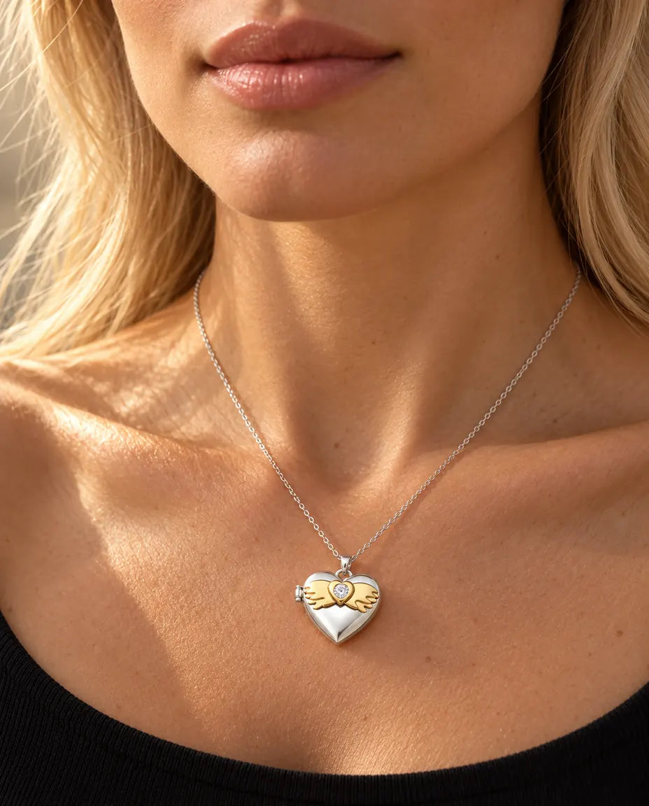 Mujer con un top negro de punto que lleva el collar relicario de corazón plateado con alas de ángel