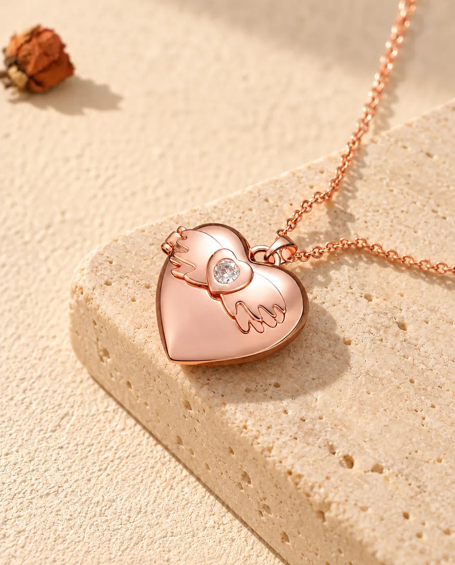 Collar relicario de corazón con alas de ángel en color oro rosa sobre travertino, con luz cálida de sol