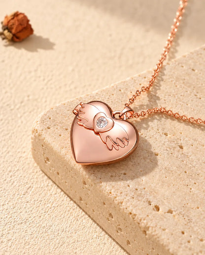Collar relicario de corazón con alas de ángel en color oro rosa sobre travertino, con luz cálida de sol