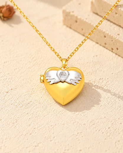 Vista frontal del relicario de corazón dorado con las alas de ángel, la circonita central y la bisagra lateral
