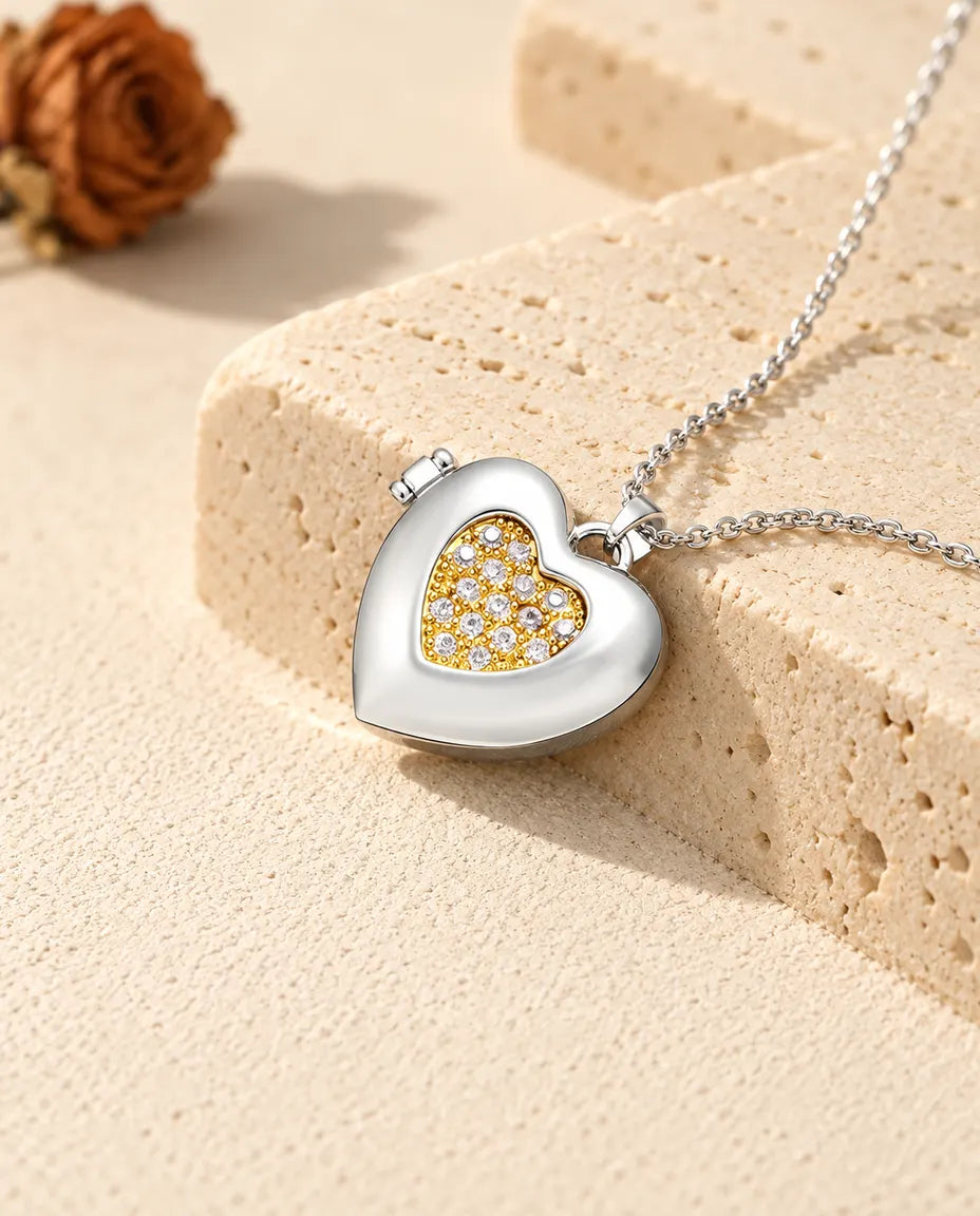 Relicario con foto de corazón plateado con un corazón interior dorado de circonitas, apoyado en un bloque de travertino