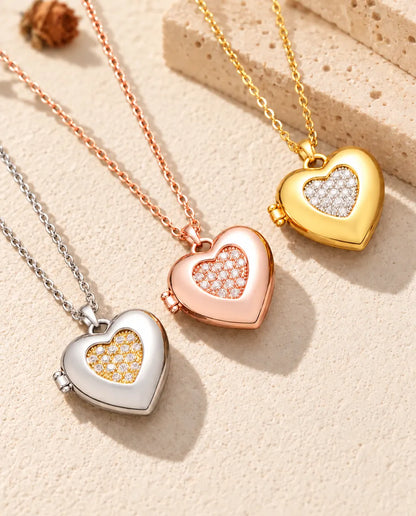 Relicarios de corazón con centro de circonitas en plateado, color oro rosa y dorado, colocados en diagonal sobre yeso crema