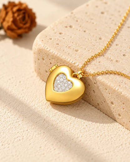 Collar relicario de corazón dorado con corazón interior plateado, apoyado en un bloque de travertino