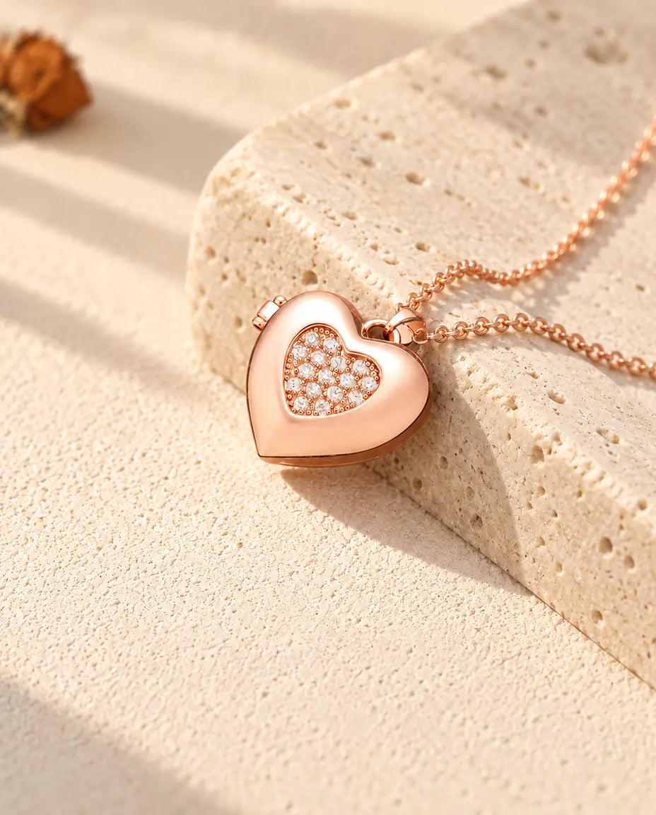 Collar relicario de corazón con centro de circonitas en color oro rosa sobre travertino, con luz cálida de sol