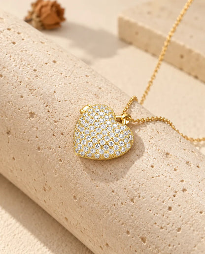 Collar relicario de corazón dorado cuajado de circonitas, apoyado en un bloque de travertino