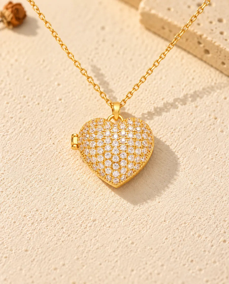 Vista frontal del relicario de corazón dorado con la tapa cuajada de circonitas y la bisagra lateral