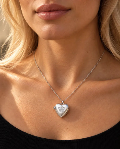 Mujer con un top negro de punto que lleva el collar relicario de corazón plateado con estrella de circonitas
