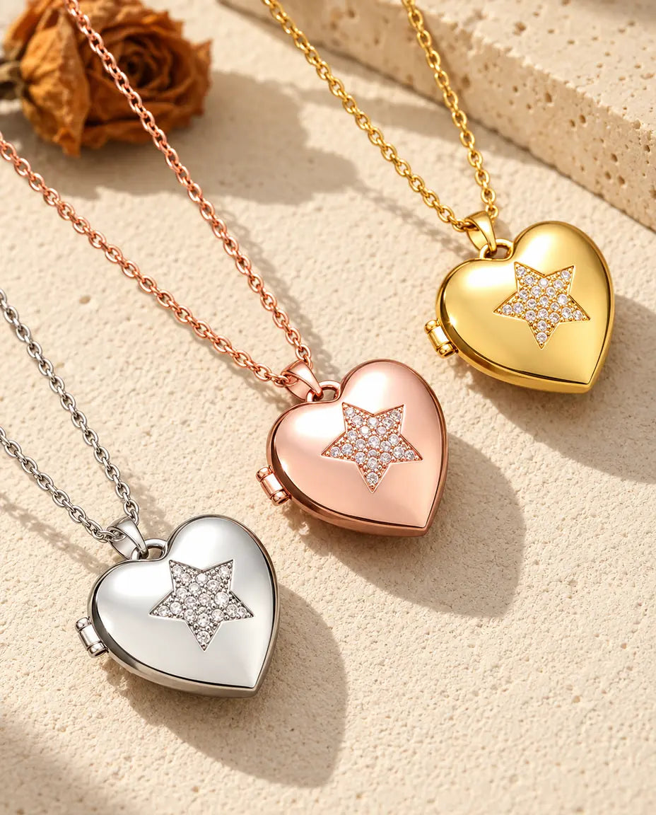 Relicarios de corazón con estrella de circonitas en plateado, color oro rosa y dorado, colocados en diagonal sobre yeso crema