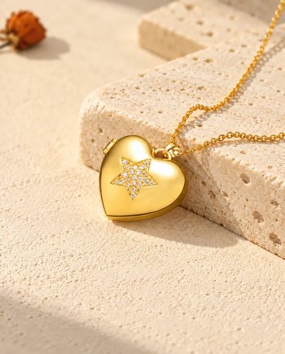 Collar relicario de corazón dorado con estrella de circonitas, apoyado en un bloque de travertino